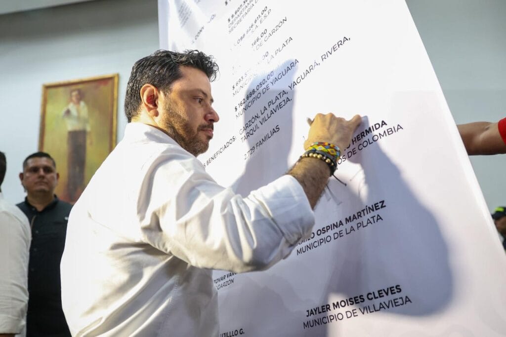 1. Hombre firmando documento oficial en evento público en La Plata, Huila, durante actividad cívica o política.