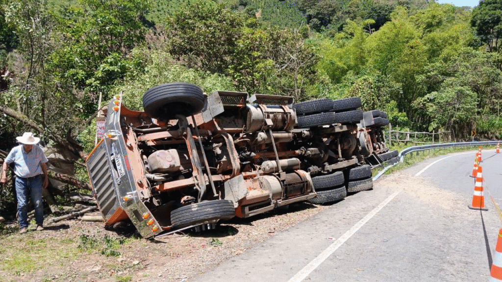 Accidente de camión volteado en carretera de Huila, Colombia, con señalización de tráfico y naturaleza verde en el fondo.