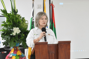 1. Mujer alcaldesa hablando en un acto oficial de la Gobernación del Huila con banderas de Colombia y del Huila en el fondo.