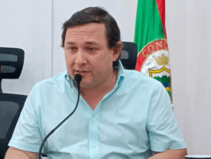 Impulsor político en Huila Tv, participando en una conferencia en un entorno formal con bandera regional en segundo plano.