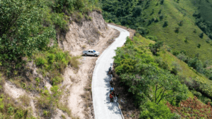 Carretera en construcción en zona montañosa del Huila, con maquinaria y trabajadores realizando trabajos de placa huella para mejorar la infraestructura vial en 12 municipios.