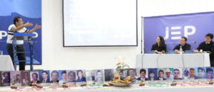 Imagen que muestra una audiencia en Huila relacionada con la investigación por falsos positivos, con panelistas y fotografías de víctimas en la mesa.