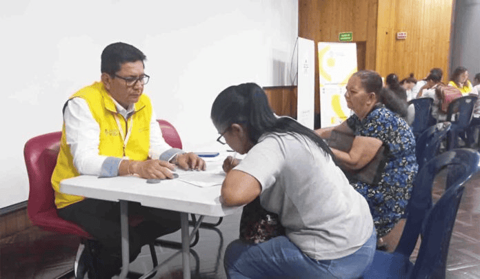 Persona atendiendo a una mujer en una oficina de Huila Tv, en un ambiente de atención al cliente, con varias personas en el fondo.