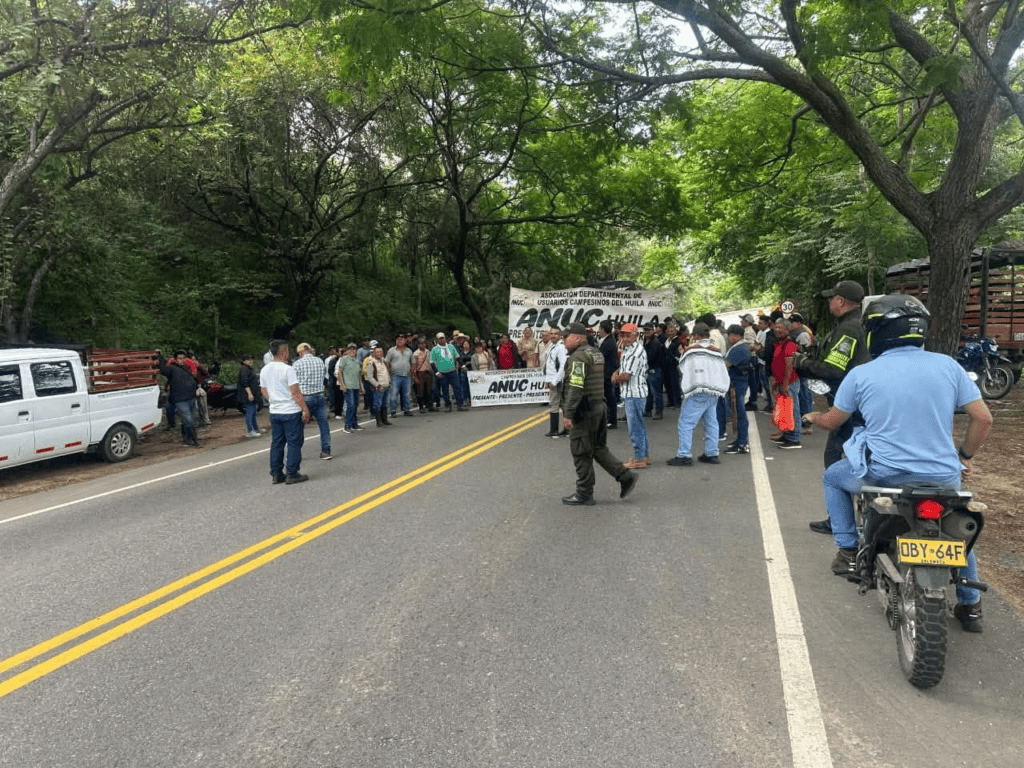 Manifestantes campesinos bloquean la vía Garzón – Neiva en protesta, con presencia de autoridades y motociclistas en un entorno natural.