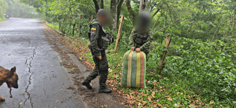 Cabo de policía revisando una bolsa en un entorno natural en Huila, Colombia, con un perro de servicio en la escena.