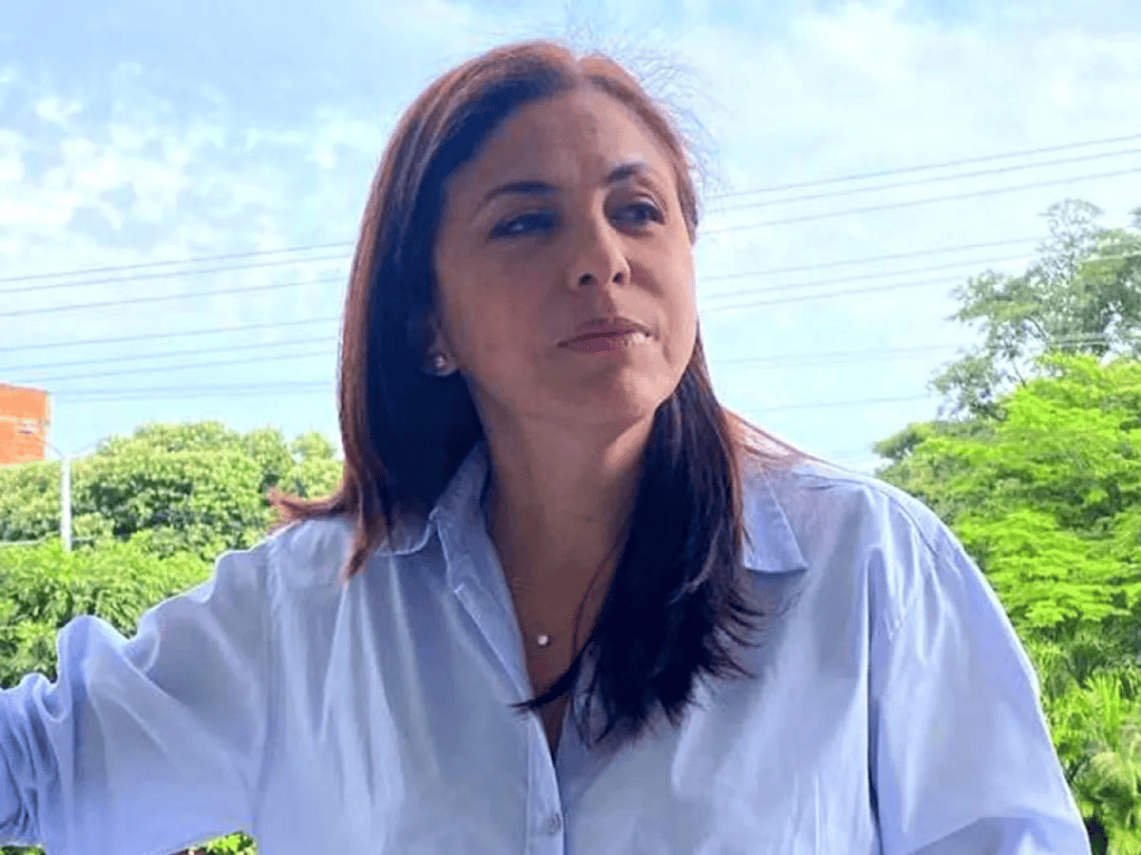 Amplia vista de una mujer con cabello castaño oscuro y blusa blanca, en un entorno natural con árboles verdes y cielo despejado, representando la belleza y cultura del Huila en Colombia.
