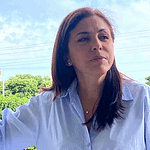 Amplia vista de una mujer con cabello castaño oscuro y blusa blanca, en un entorno natural con árboles verdes y cielo despejado, representando la belleza y cultura del Huila en Colombia.