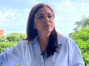 Amplia vista de una mujer con cabello castaño oscuro y blusa blanca, en un entorno natural con árboles verdes y cielo despejado, representando la belleza y cultura del Huila en Colombia.