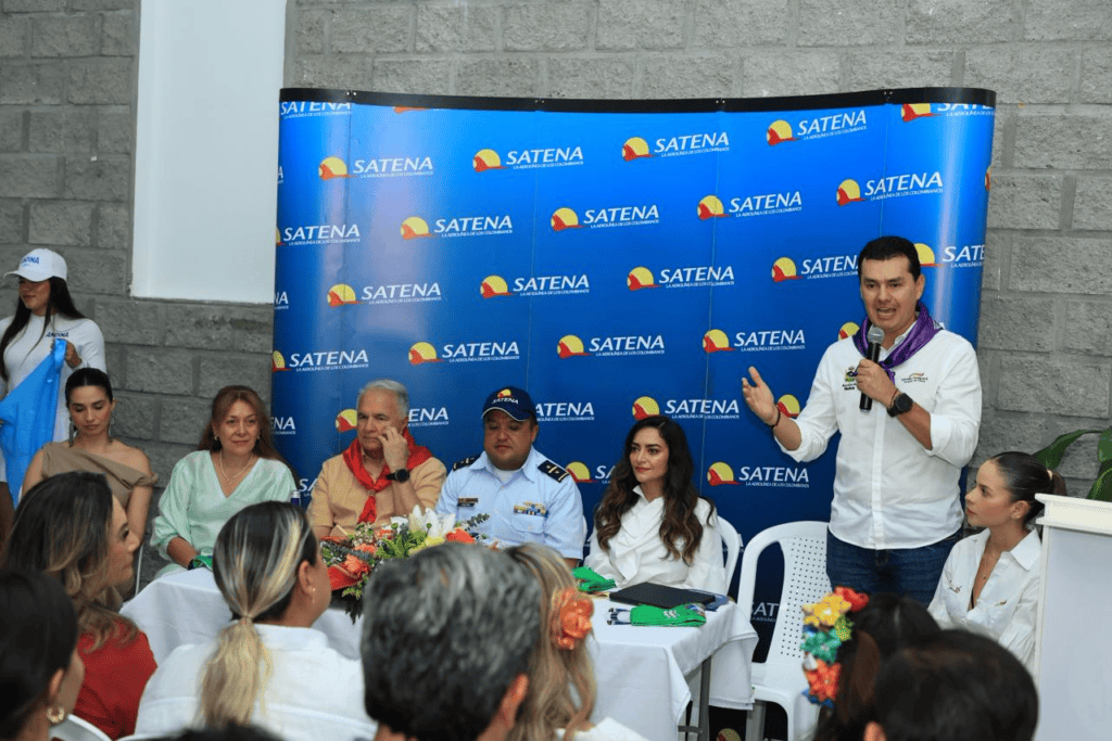 Hombre hablando en un evento de Satena con audiencia y panel de discusión en un entorno formal.