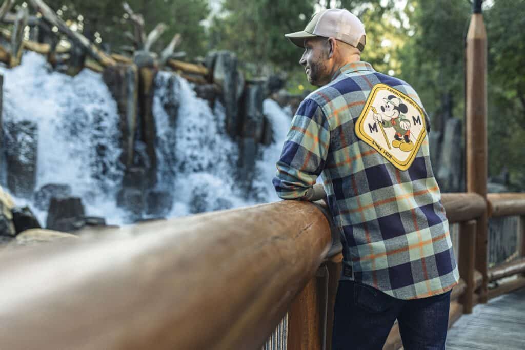 Vibrant plaid shirt with Mickey Mouse patch, exploring nature at a waterfall.