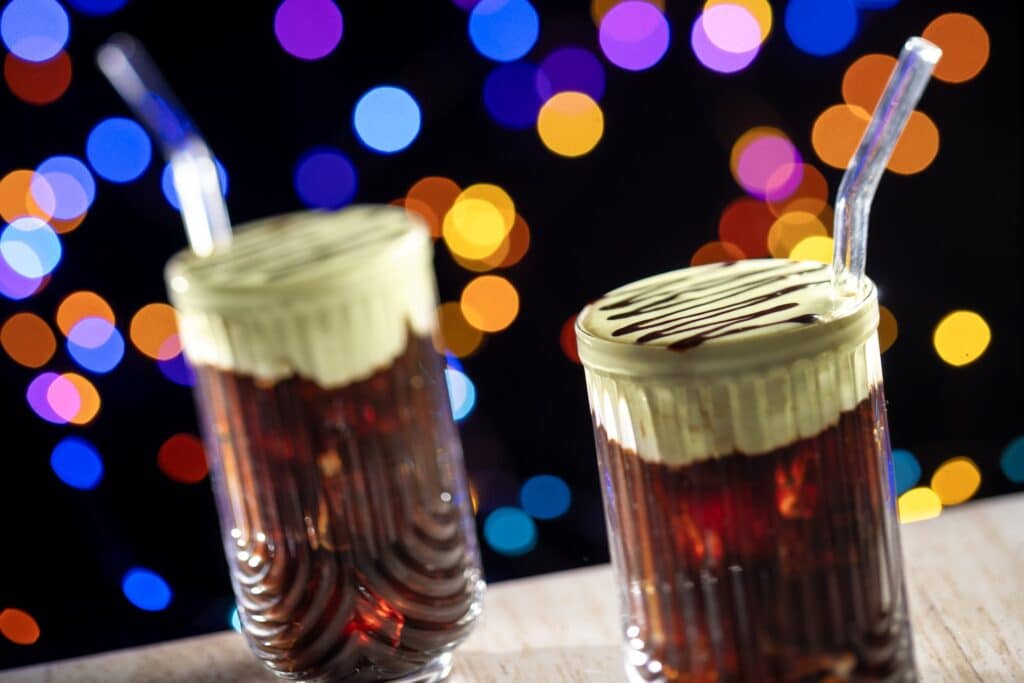 Cream soda floats with whipped cream and chocolate drizzle against colorful bokeh background.
