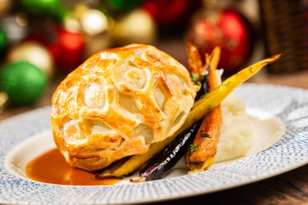 Golden roasted chicken pot pie with mashed potatoes and colorful roasted vegetables, perfect for Disney-themed holiday feasts.