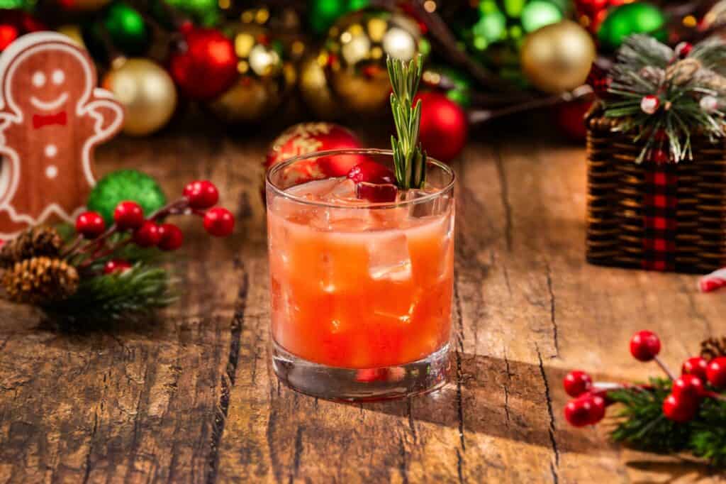 Refreshing holiday cocktail with ice, cranberries, and rosemary garnish on rustic wooden table.