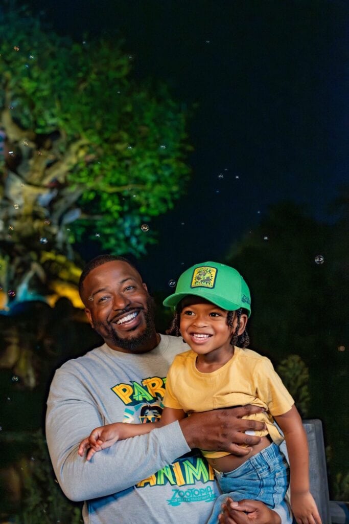 Brightly lit tree at night with a smiling man holding a happy young girl in front of a dark sky.