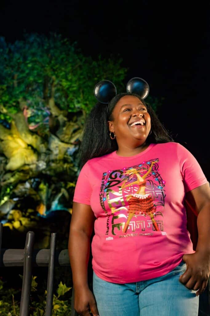 Mickey Mouse ears headband, pink Disney T-shirt, and joyful expression at Disney theme park night.