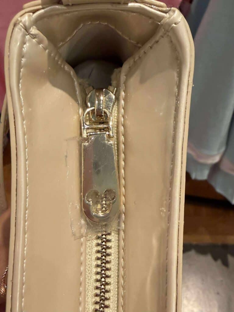 Mickey Mouse zipper pull with gold accents on a beige designer bag.