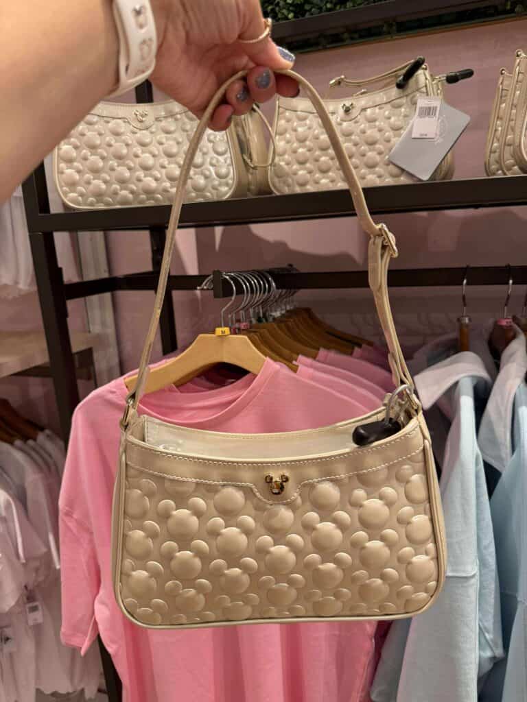 Beige Mickey Mouse head embossed handbag with gold hardware and adjustable strap.