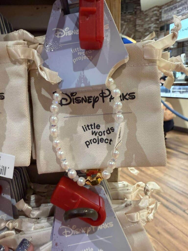 Daisy Disney Little Words Project necklace with pearls and Minnie Mouse charm on beige bag.