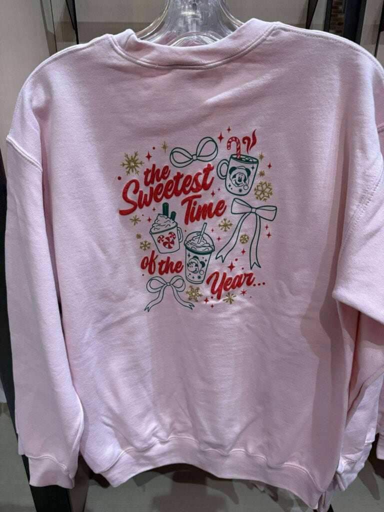 Cozy pink holiday sweatshirt featuring festive design with drinks and Christmas ornaments, perfect for Disney fashion lovers during the season.