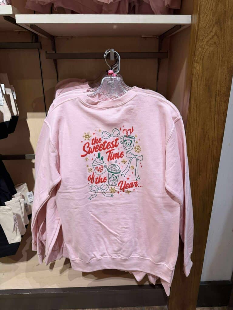 Pink Christmas sweatshirt with holiday drinks and festive message.