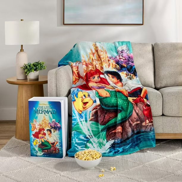 Disney The Little Mermaid blanket featuring Ariel, Flounder, and Ursula on a cozy sofa in a modern living room setting.
