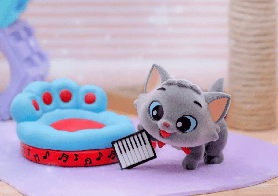 Adorable plush gray cat with big eyes next to a music-themed paw print pet bed. Perfect for Disney-inspired pet accessories and décor.