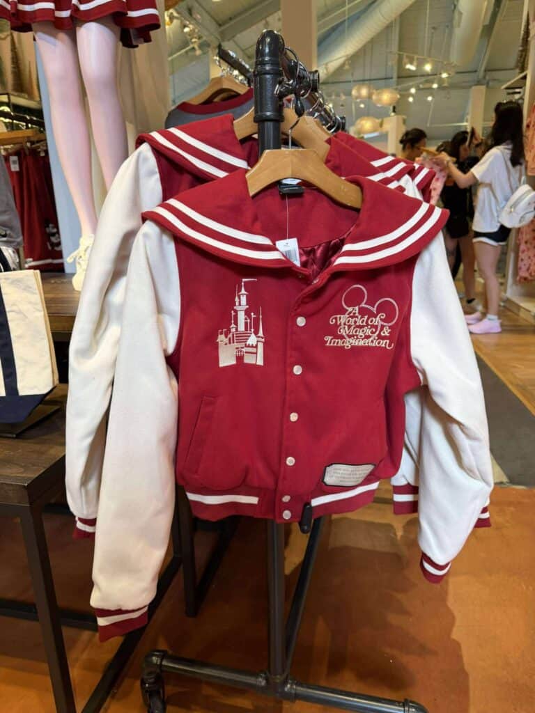 Red and white Disney-themed varsity jacket with castle embroidery and "World of Magic & Imagination" text.