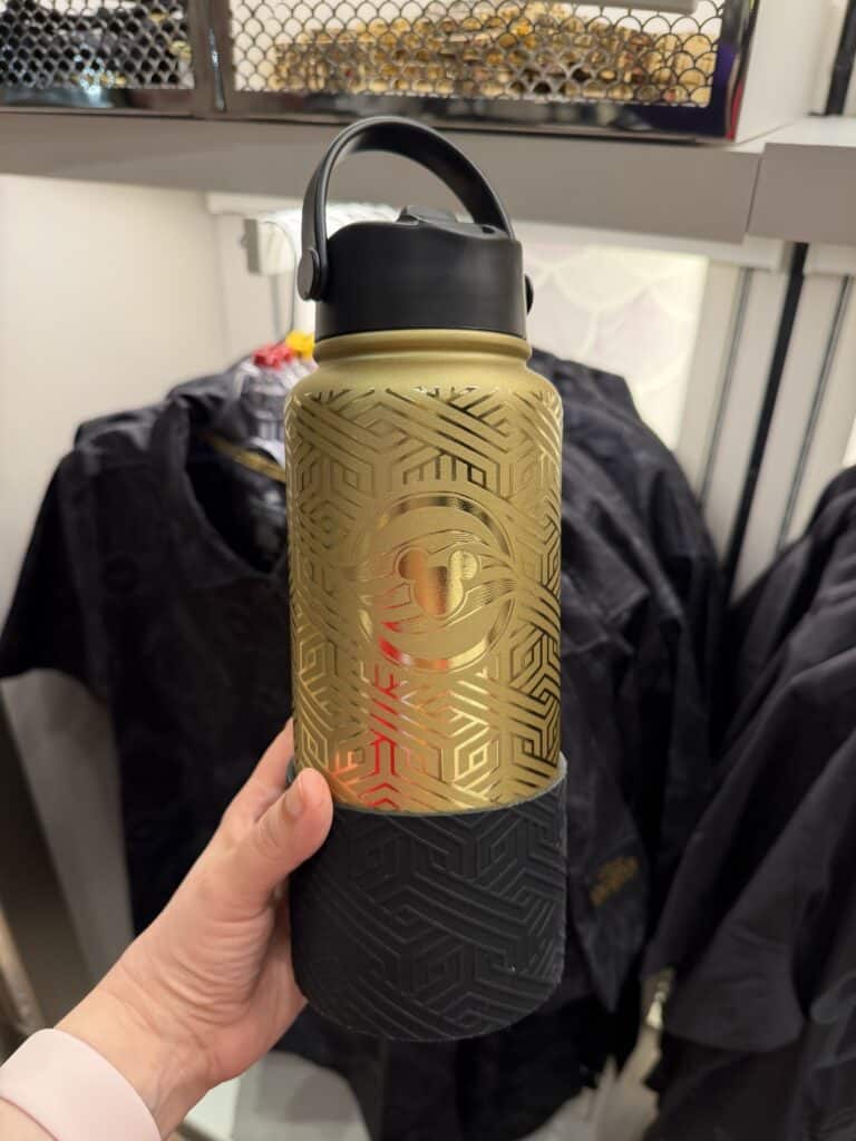 Disney water bottle featuring gold geometric pattern and a smiling face logo, perfect for Disney enthusiasts.