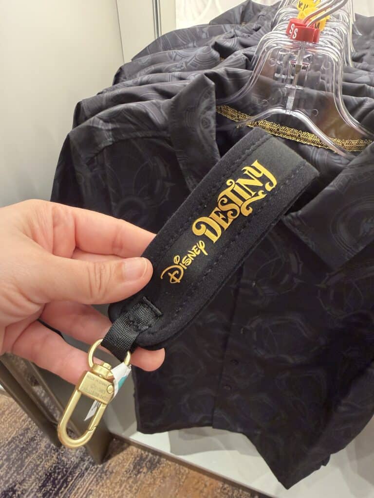 Close-up of a Disney Fashionista-themed black lanyard with gold logo detail, accessories, and hangers for Disney apparel.