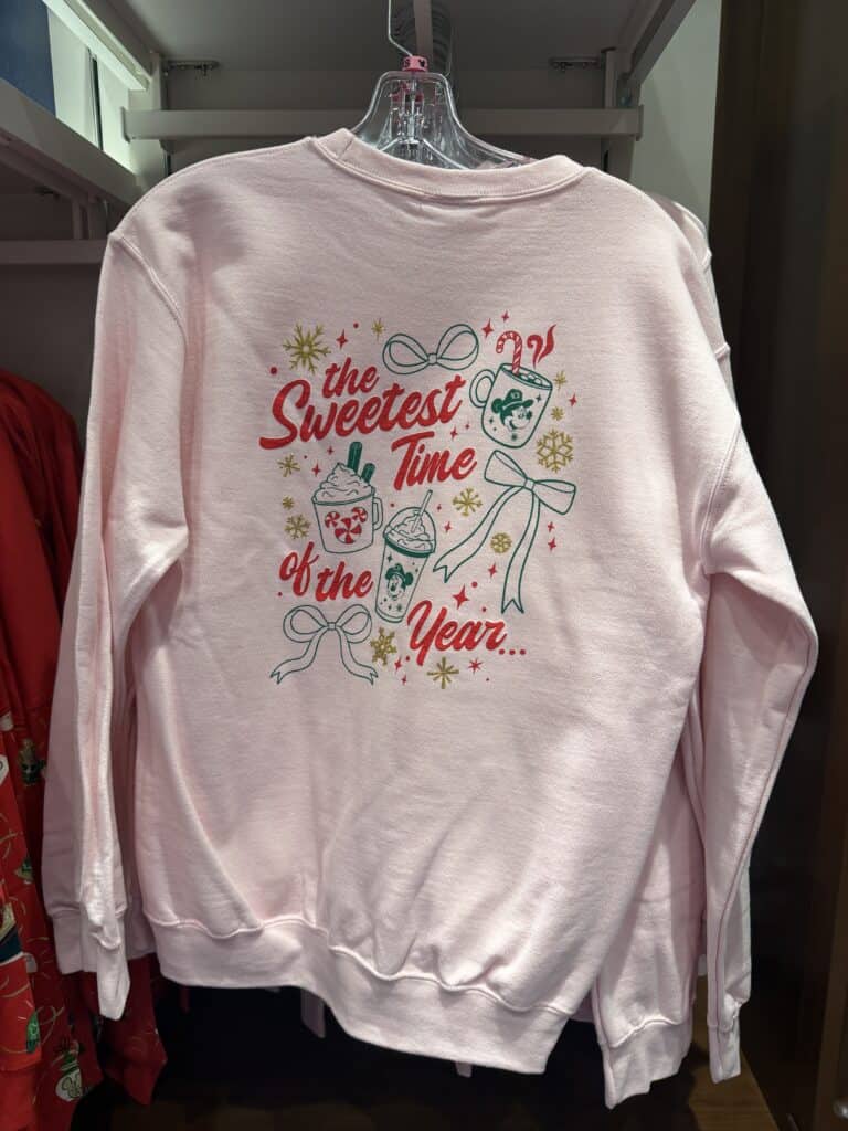 Cute Disney-themed pink sweatshirt for Christmas season, featuring drinks, snowflakes, and festive text.