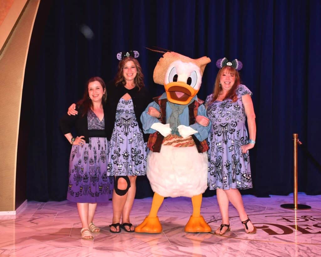 Disney fans dressed in Disney-themed fashion posing with Donald Duck in a themed event setting.