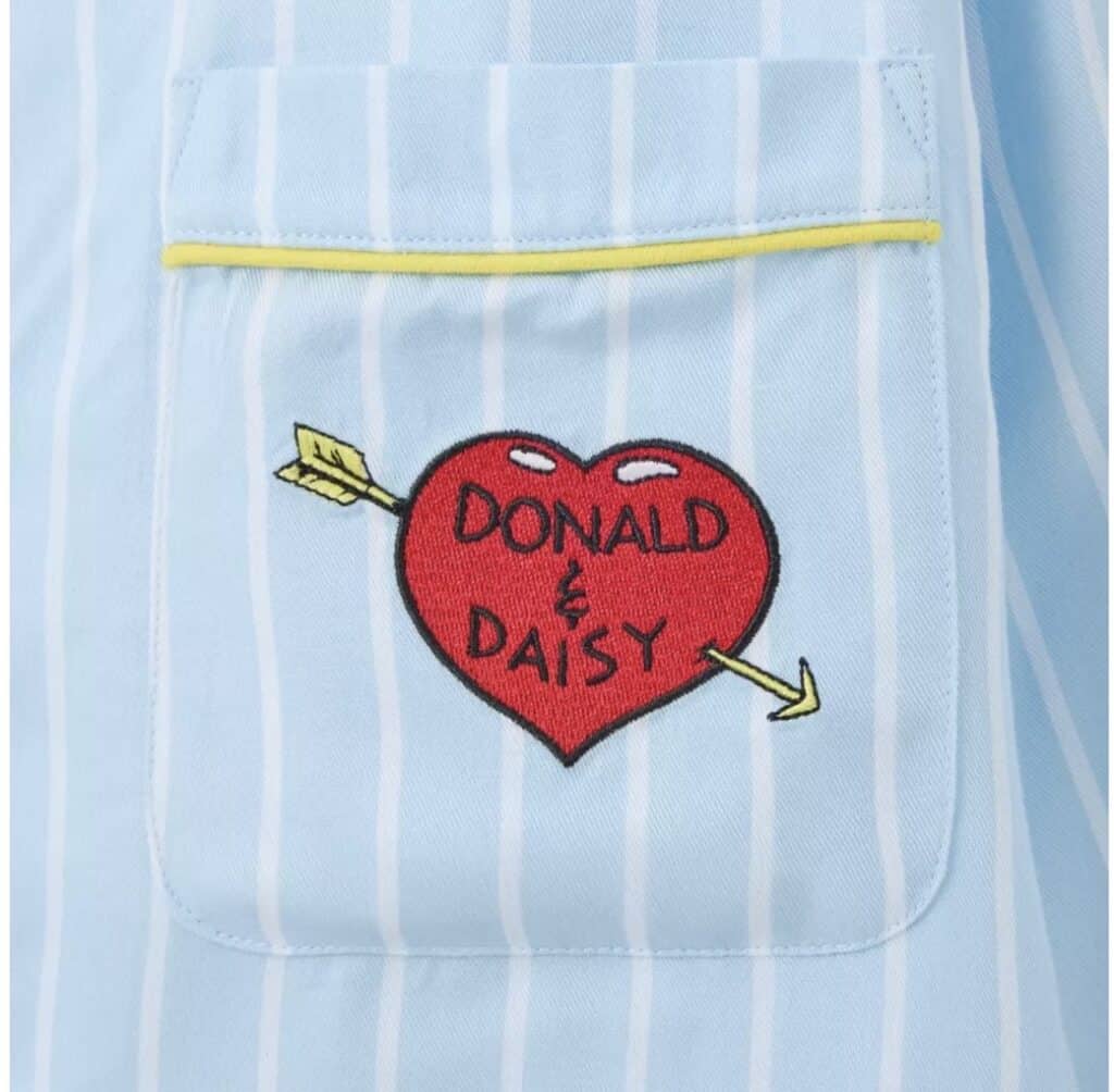 Colorful embroidered heart patch with arrows on light blue striped fabric.