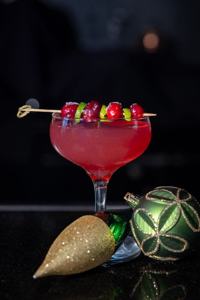 Vibrant red holiday cocktail garnished with cherries and lime slices. Perfect for Disney-inspired celebrations.