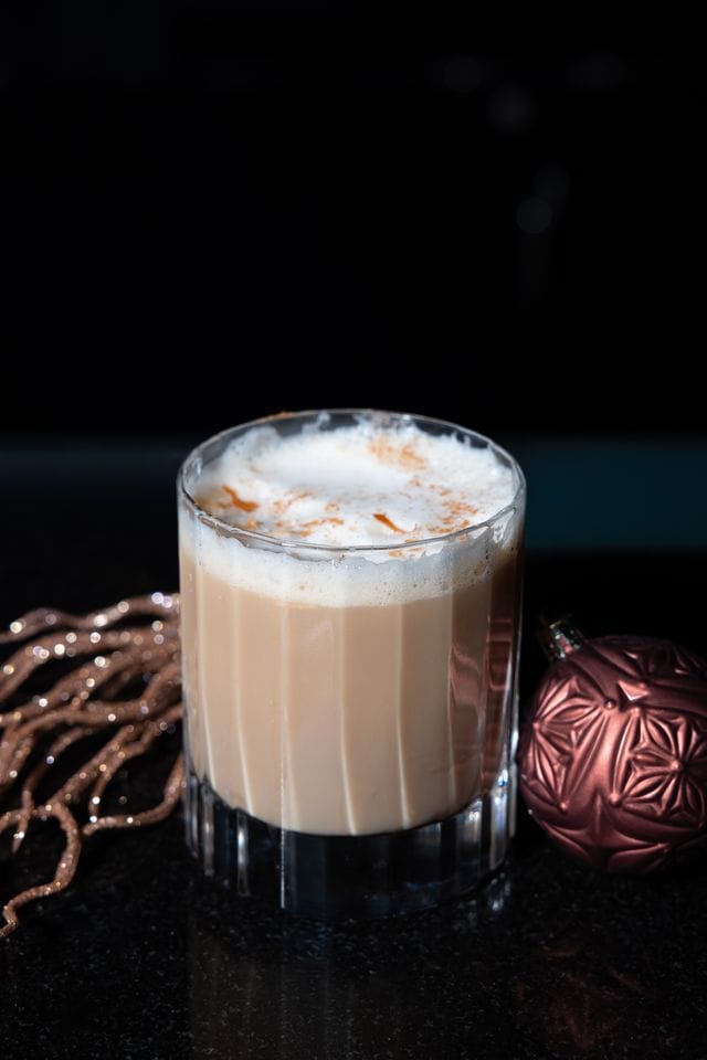 Creamy holiday eggnog with a sprinkle of cinnamon in a clear glass.