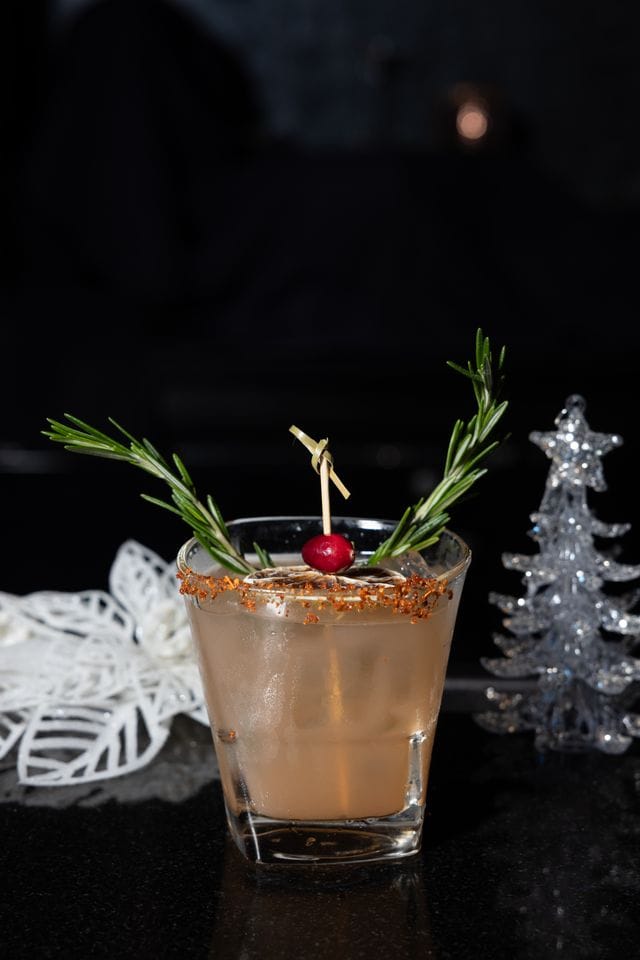 A sparkling holiday cocktail garnished with rosemary sprigs and a cherry, perfect for Christmas celebrations.