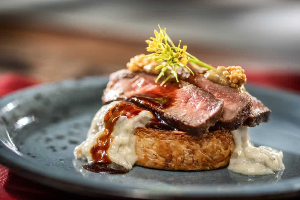 Gourmet beef entrée with mashed potatoes, herbs, and sauce, styled for a fine dining experience.