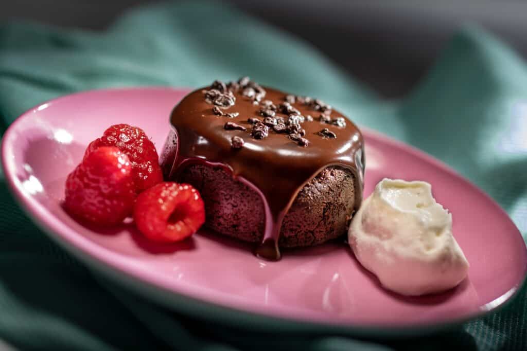 Rich chocolate lava cake with a gooey center, garnished with chocolate shavings, served with raspberries and whipped cream.