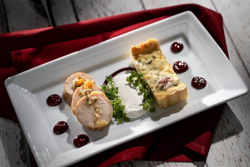 Delicious chicken roulade with cheese filling, served with berry sauce and fresh herbs on a white plate.