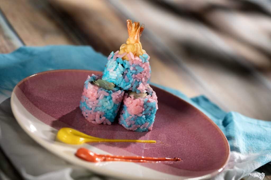 Vibrant sushi rice with shrimp tempura, served on a pink plate with mustard and ketchup. Perfect for Disney food fans.