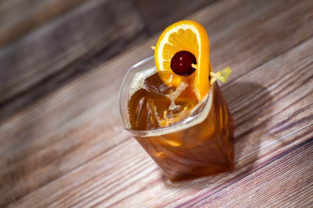 Bright orange cocktail garnished with orange slice and cherry, served over ice in a glass.