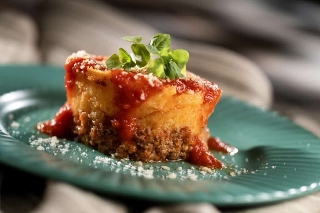 Vibrant cheesecake topped with tomato sauce and herbs, served on a stylish teal dish.
