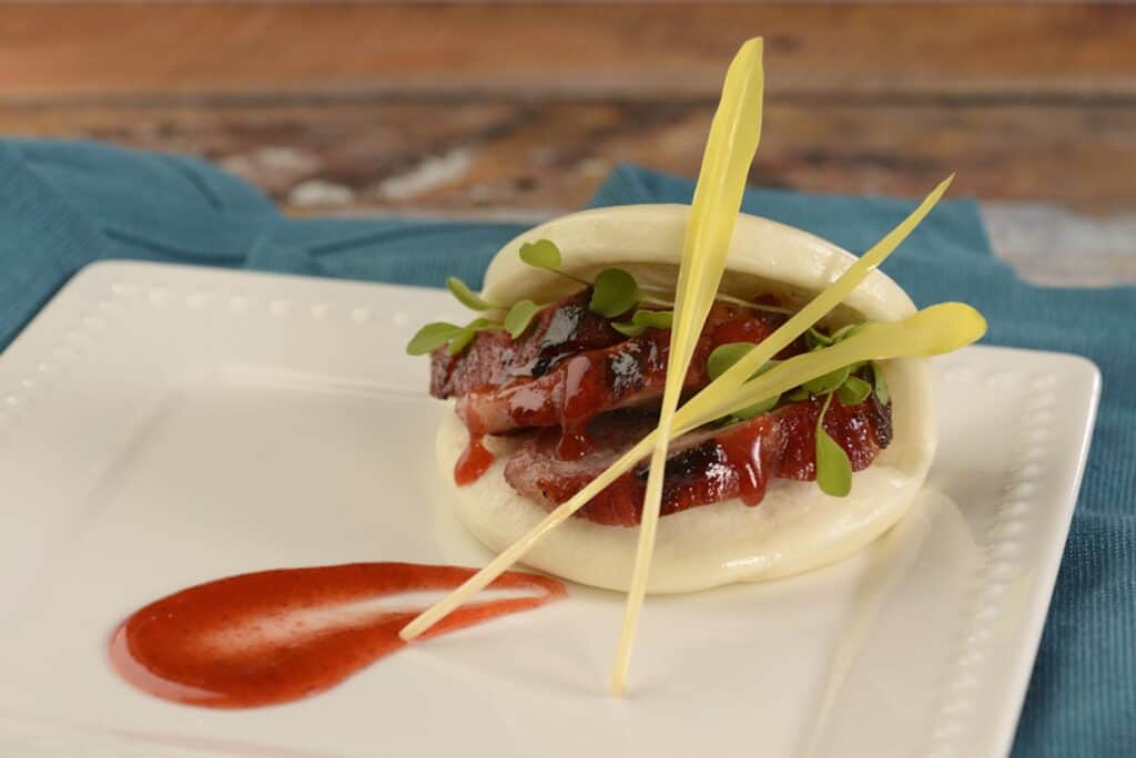 Close-up of a gourmet lamb slider with fresh greens, tomato sauce, and decorative garnishes.