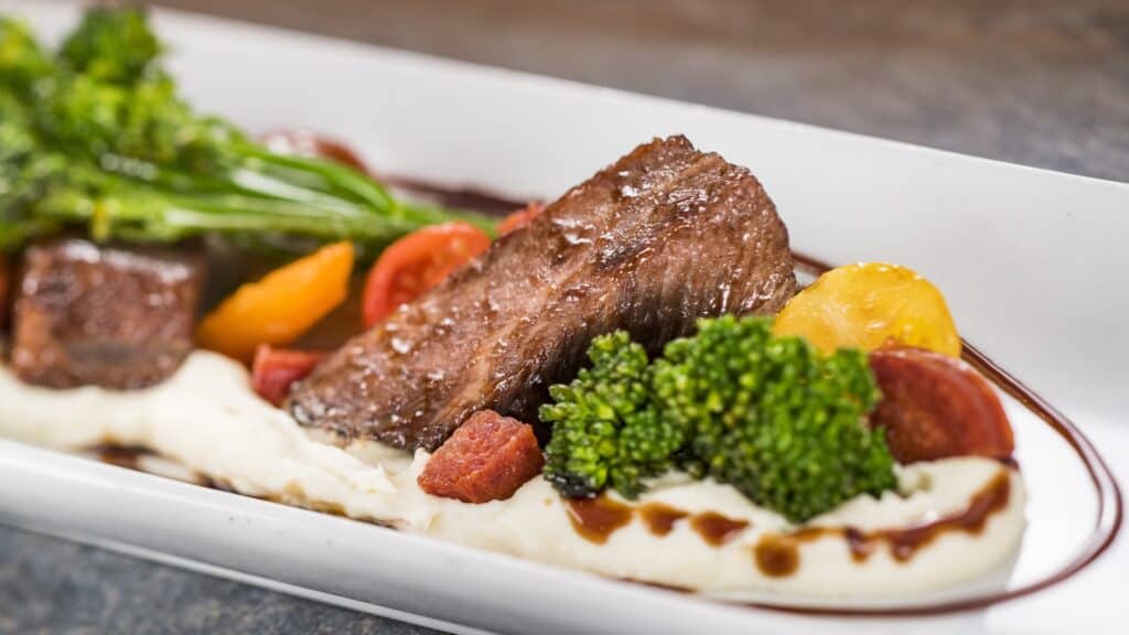 Steak dinner with vegetables, mashed potatoes, and sauce on a white plate, perfect for gourmet food lovers.