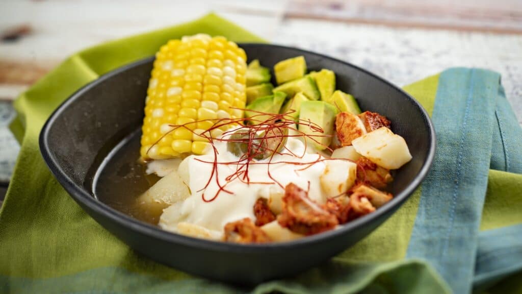 Vibrant Mexican food featuring corn, avocado, potatoes, and seasoned chicken served in a black skillet.