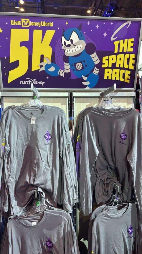 Bright gray long-sleeve shirts with "5K runDisney" space-themed graphics displayed on hangers.