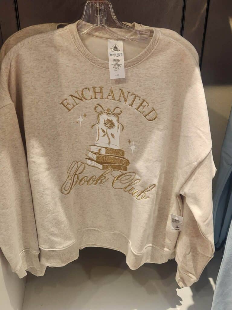 Soft cream crewneck sweatshirt with gold embroidery design featuring stacked books and a rose.