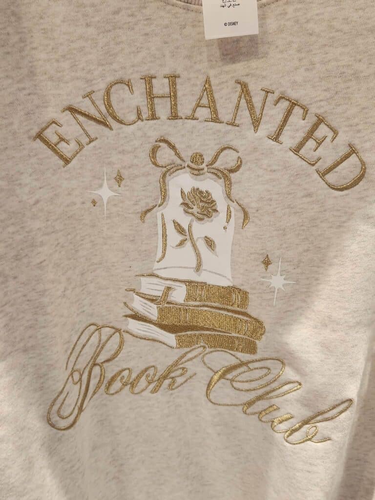 Disney fashion sweatshirt featuring "Enchanted Book Club" text with star details.