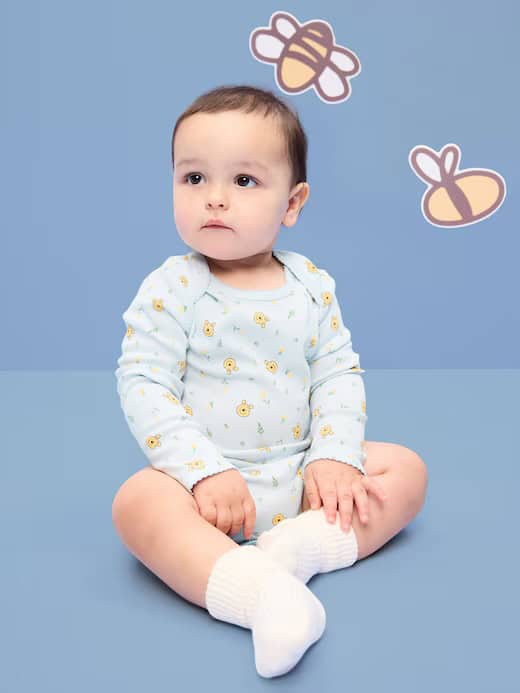 Baby girl in yellow chick pajamas sitting on blue background with bee wall decals.