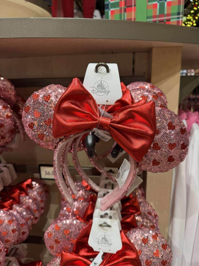 Bright pink Minnie Mouse ears headband with red satin bow and heart decorations, ideal for Disney lovers.
