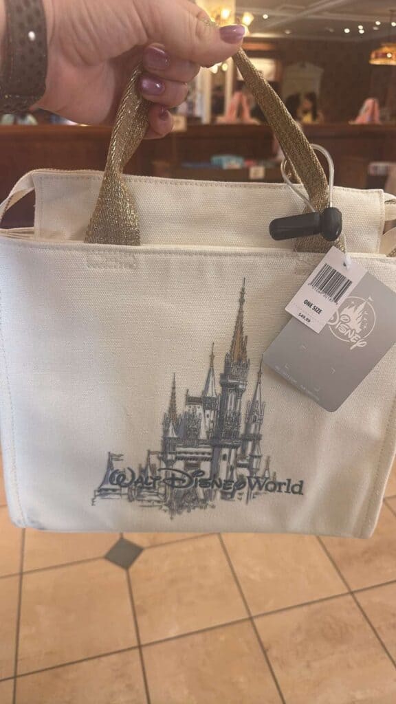 A white Disney World tote bag featuring a castle graphic and gold handles, perfect for Disney enthusiasts.